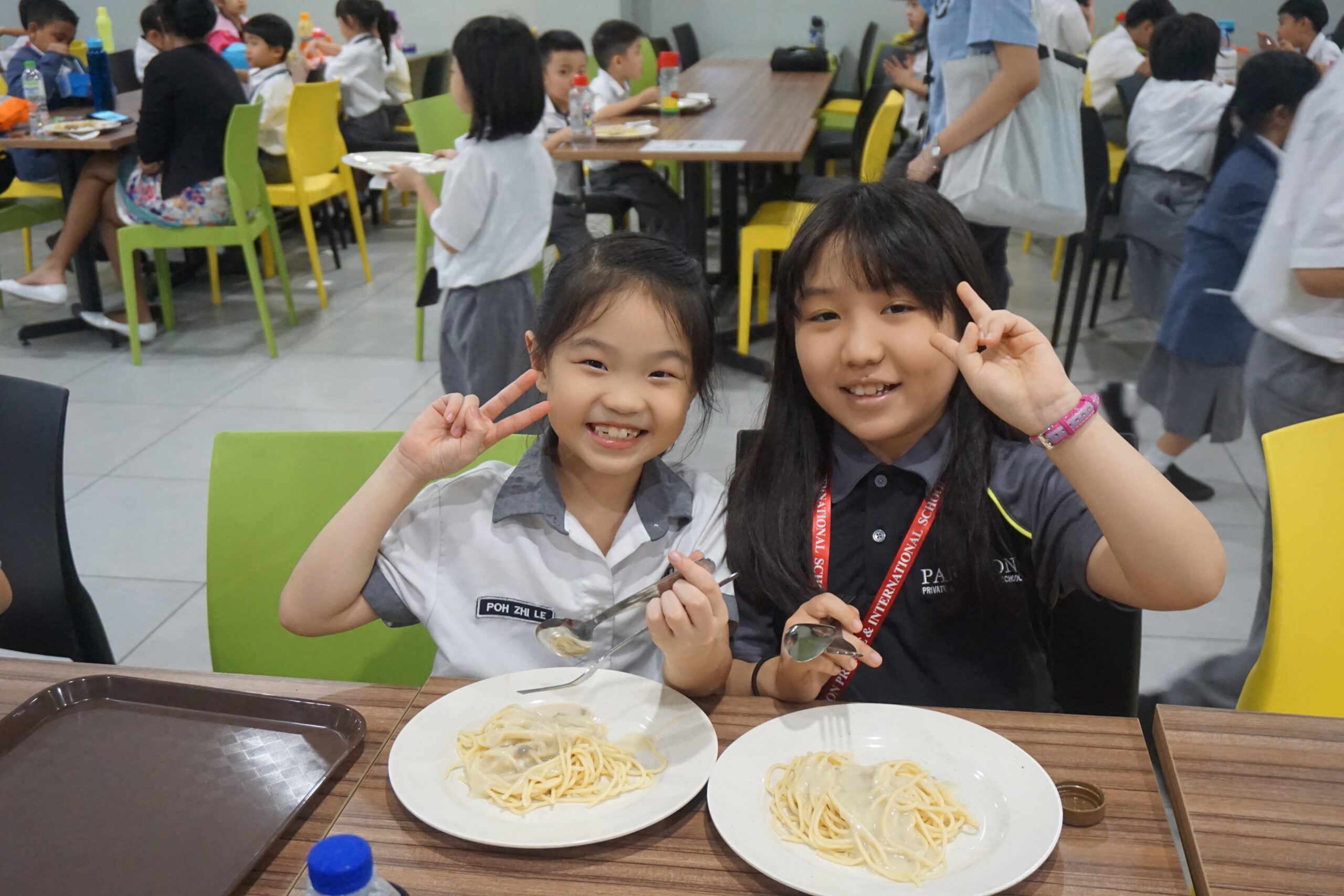국제학교 식당에서 교복을 입은 두 학생이 파스타 점심을 먹으며 웃는 모습