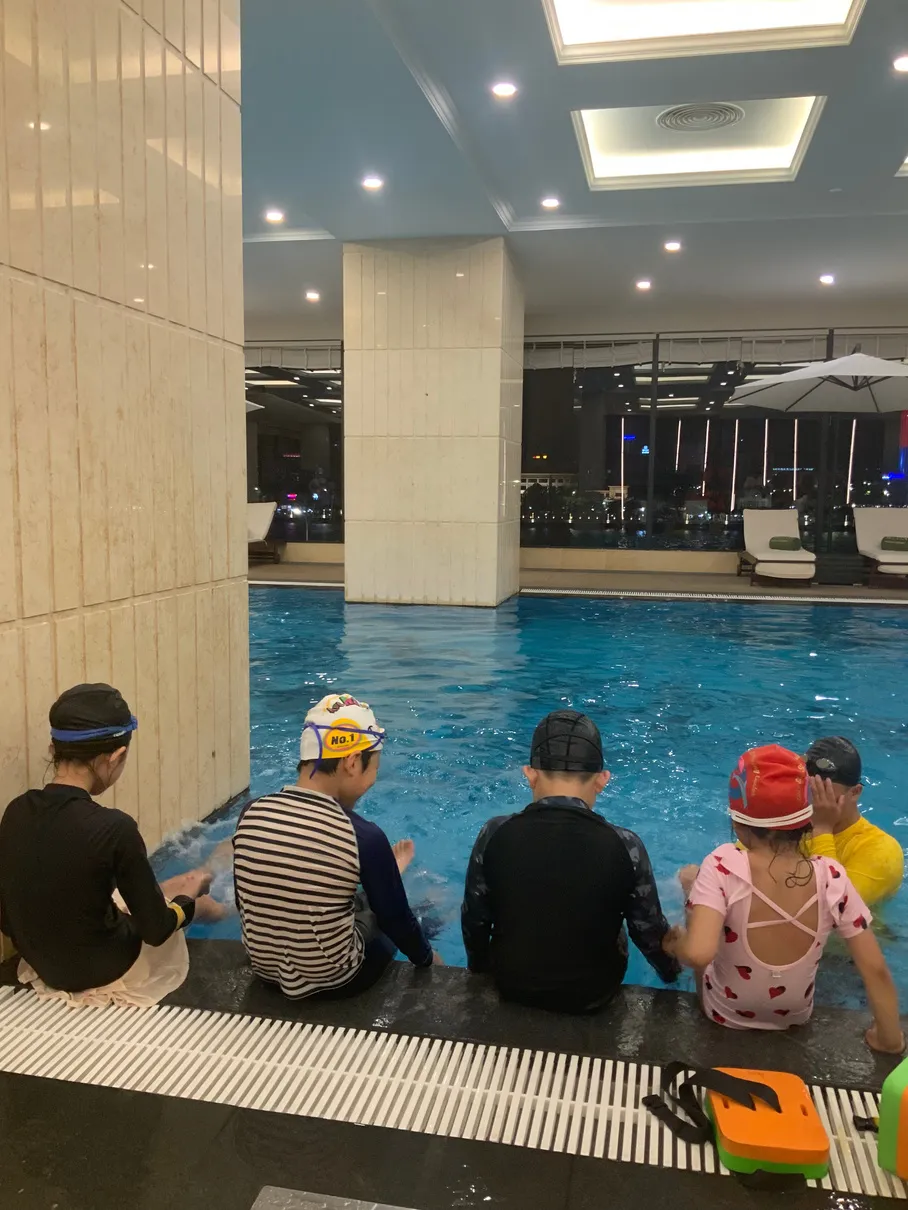 호텔 실내 수영장 가장자리에 앉아 수영 레슨을 기다리는 수모 쓴 아이들
