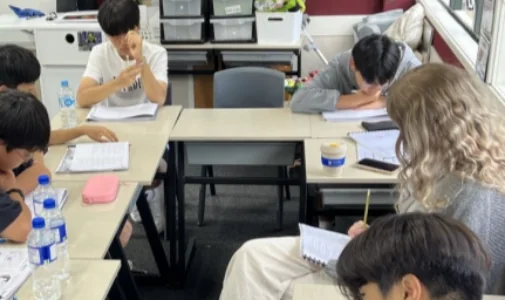 학생들이 긴 책상에 앉아 필기하며 수업을 듣는 장면